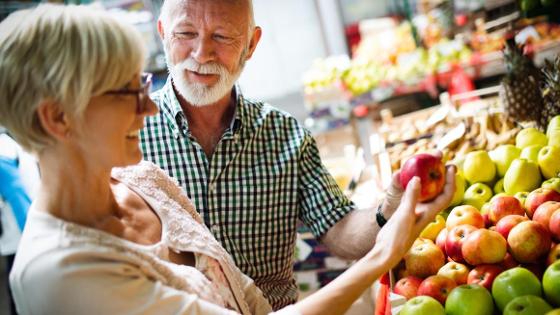 Ein Paar beim Einkaufen von Obst auf einem Markt. Die Frau im Vordergrund hält einen Apfel in der Hand.